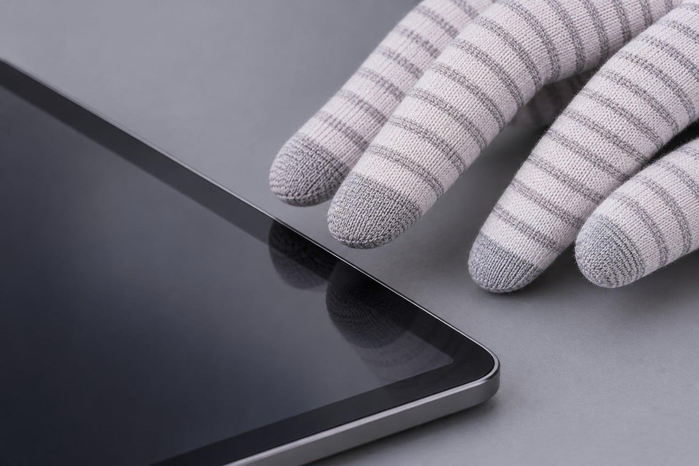 Gray striped glove fingertips beside a tablet edge